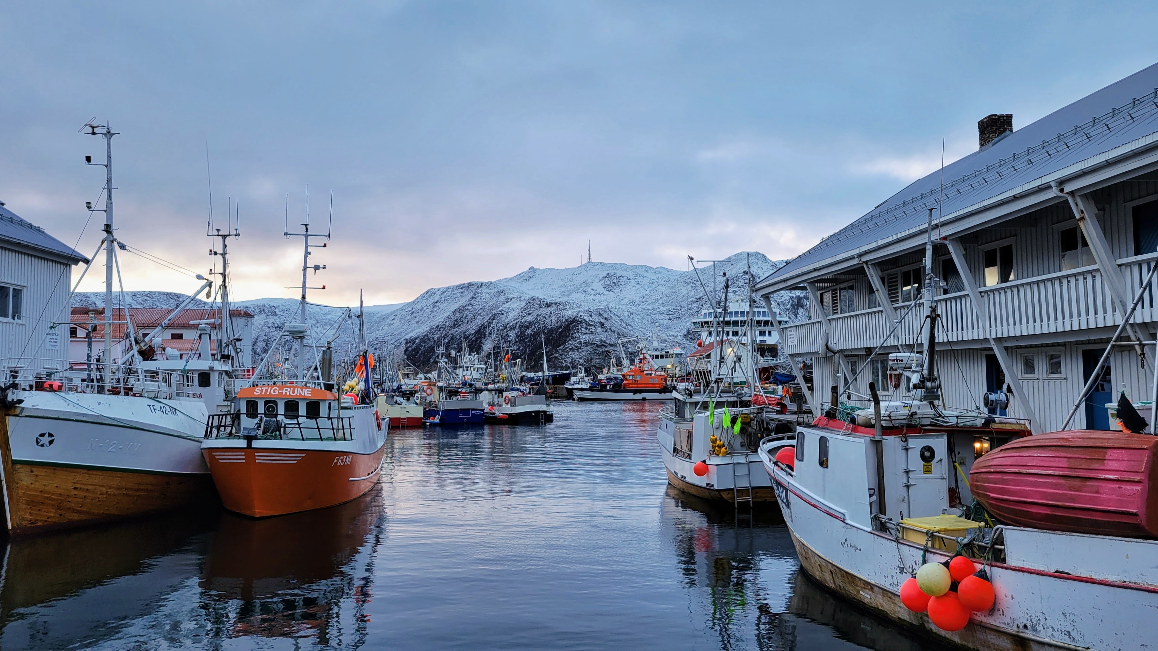 Colorful fishing boats moored in the harbor at Honningsv&aring;g, Norway, with mountains behind